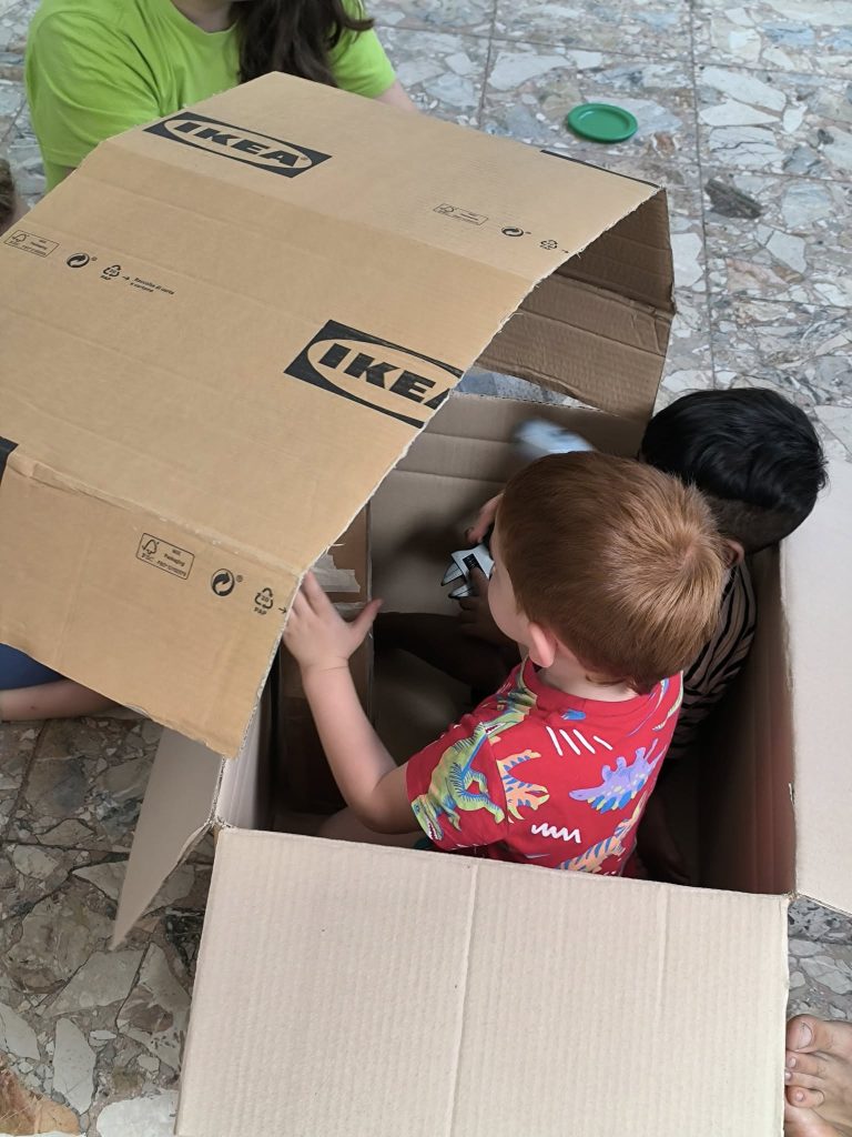 Bimbi e bimbe che giocano con oggetti semplici come scatole e fili